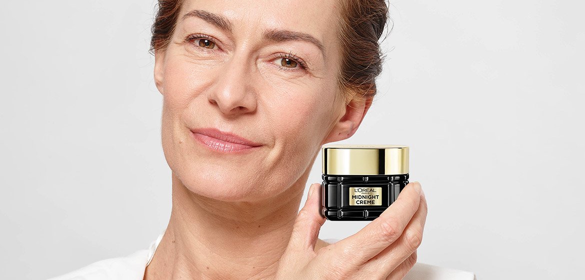 Eine Frau haelt L'Oréal Midnight Creme neben ihrem Gesicht